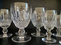 Six cut-crystal glasses with diamond pattern and hexagonal stems arranged on shelf