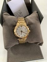 Watch displayed on grey cushion inside open Bulova black box showing gold-tone case and silver dial