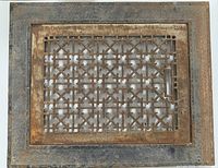 Full view of the antique iron floor grate with decorative geometric pattern framed by textured iron edges showing surface rust and patina.