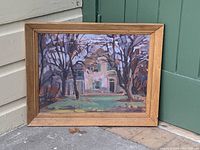 Vintage framed oil painting of a house with trees, showing front view with the painting resting against a green door and beige siding.