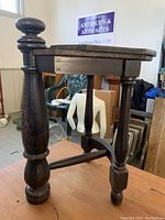 Small vintage wooden side table with turned legs and a large rounded finial on one corner, showing wear consistent with age and use.