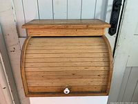 Front closed view of wooden roll top bread box showing curved slatted door and white knob