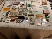 Full display of coins, paper money, ephemera, postcards, toy vehicles, and other collectibles arranged on table