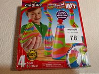 Box front showing colorful sand art on 4 bottles and child holding one. Box has minor bottom edge damage.