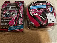 Photo showing the Monster High 2.1MP digital camera and Monster High volume limiting headphones both in clear packaging with graphics and logos visible.