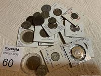 Coins in white 2x2 holders and loose coins arranged on beige fabric. Visible handwritten labels indicating origin and dates such as Philippines, Great Britain, France.