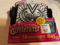 Front view of Glitterazzi messenger bag still in packaging showing black and white owl design and included permanent markers.