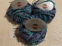 Three skeins of Hip Hop Skacel yarn made in Italy in blue and purple blend, showing label and yarn texture.