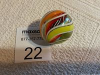Large glass marble showing colorful swirls inside, placed on a carpet next to a MaxSold lot number card.