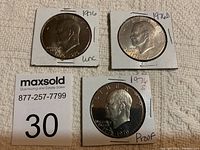 Photo of three Eisenhower dollar coins from 1976: uncirculated Philadelphia, Denver of uncertain condition, and San Francisco Proof, all in cardboard holders with handwritten labels.