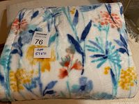 Folded throw blanket with visible floral pattern and size label on top