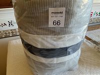View of rolled and sealed queen size quilt with grey and white stripes pattern inside plastic bag, showing label with lot number 66.
