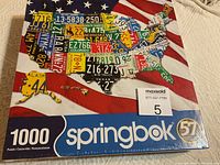 Front image of unopened Springbok 1000 piece puzzle box showing US map composed of license plates on American flag background.