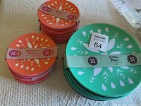 Stacked orange and pink appetizer plates with white leaf pattern on left and stacked green dinner plates with white leaf pattern on right.