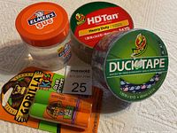 Photo showing Elmer's glue jar, Gorilla Kids glue sticks, Duck Heavy Duty Tan tape roll, and Duck decorative tape roll with hearts pattern.