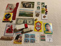 Full lot arranged on fabric featuring stamps, coins, collectible cards, silver certificate, plastic figures, and other paper memorabilia.