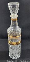 Front view of vintage cut glass decanter showing its stopper, intricate cut glass design, and gold floral band detail.