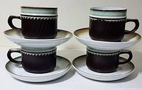 Four Denby-Langley Rondo stoneware dark brown textured tea cups each placed on matching green to white gradient saucers, arranged in two rows, cups have rounded handles and smooth glazed rims.