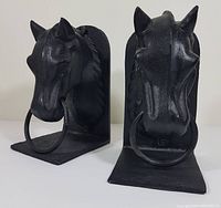 Pair of black cast steel horse head book ends with metal rings, showing front and slight side view, highlighting detailed horse features and textured finish.