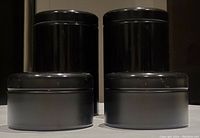 Set of four black metal cannisters with lids, including two tall and two short pieces, shown against a dark background.