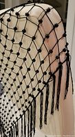 Close-up image showing the black beaded diamond pattern and fringe trim of the shawl draped over a white chair.