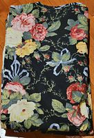 Folded cotton fabric drapery panel displaying the floral print on black background, laid on wood floor for scale and condition inspection.