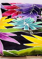 Close-up of bright floral patterned rayon tablecloth on black background, showing purple, yellow, teal, green, and red flower details.