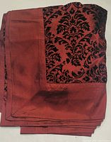 Photo of folded burgundy tablecloth showing black velveteen damask accent design on fabric corner.
