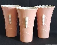 Front view of the three pink Fire King Vitrock vases showing embossed leaf and bead pattern with scalloped white rim.
