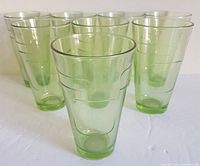 Eight vintage green drinking glasses arranged on white surface showing overall lot condition and design.