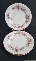Four stacked dinner plates with floral pink and purple rose pattern and gold trimmed edges, shown against a dark background.