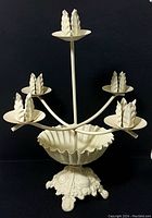 Full side view of the wrought iron painted cream white tiered candle holder with bowl base and ornate footed stand showing five arms holding drip plates with leaf prongs.