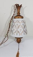 Full view of vintage hanging light fixture showing white glass shade with gold floral patterns, gold-tone metal hardware, chain, and tassel pull
