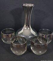 Vintage mercury glass decanter with four matching tumblers arranged in front, showing overall set with silver fade finish.