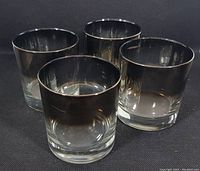 Front-facing view of four low ball glasses with mercury silver fade finish arranged in a pyramid shape on black background.