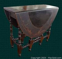 Closed position of antique black japanned drop-leaf gateleg table showing turned legs and drawer below top.