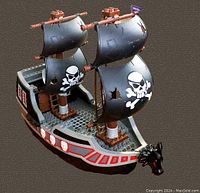 Photo showing front side angle of the pirate ship with black sails and skull and crossbones graphics, red and white skull detailing on hull, brown masts, and dragon figurehead at front.