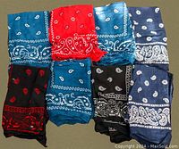 Photo showing eight folded bandannas in various colors including blue, red, black, and dark blue with white or red paisley patterns.