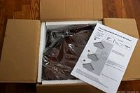 Open box showing the unassembled wooden corner wine rack inside packaging with styrofoam and a printed assembly instruction sheet.