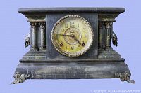Front view of entire clock showing black stained wood, faux marble columns, gilt clock face, and decorative metal feet.