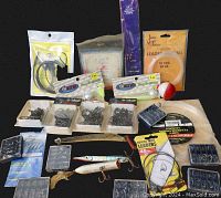 Photo showing assorted fishing hooks, fishing leaders, nylon fishing line, fishing lures, swivels and a bobber arranged on a black background