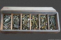 Top view of wooden box with sliding lid open revealing six compartments filled with assorted nuts, bolts, screws, and other hardware pieces.