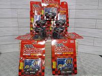 Front view of nine packaged 1997 Bill Elliott Racing Champions 1:64 scale NASCAR diecast cars arranged in pyramid style on a wood panel backdrop. Car paint pattern is McDonald's blue with yellow and red trim, and number 94 on roof and sides.