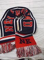 Navy blue scarf featuring large red and white lettering spelling 'NEW ENGLAND' with tassel fringes.