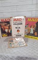 Four vintage magazines in photo: three Mad magazines and one Cracked magazine, all sealed in plastic and backed by cardboard.
