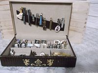 Full view of the open decorative box containing multiple tie clips secured by a strap on the lid and cufflinks arranged in compartments