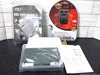 Photo showing all items in the lot: GPX MP3 player in red and black packaging, PNY USB card reader in sealed box, Merlin power bank and manual.
