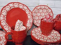 Photo showing 10" and 8" red and white patterned plates along with red mugs and napkins inside mugs.