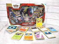 Image of the sealed Darkrai VStar Premium Collection box with visible booster packs and a spread of loose Pokémon cards in front.