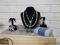 Full lot of mixed silver-tone jewelry including necklaces, earrings, pins, and bracelets arranged on a display stand and flat surface.